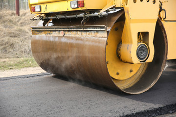 asphalt paving works. water is steaming on a cylinder of the asphalt paver