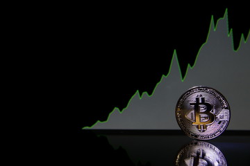 Bitcoin on the background of bullish stock chart on a black background. cryptocurrency coin on black background with reflection. increase in the value of bitcoin, dark background with copy space.