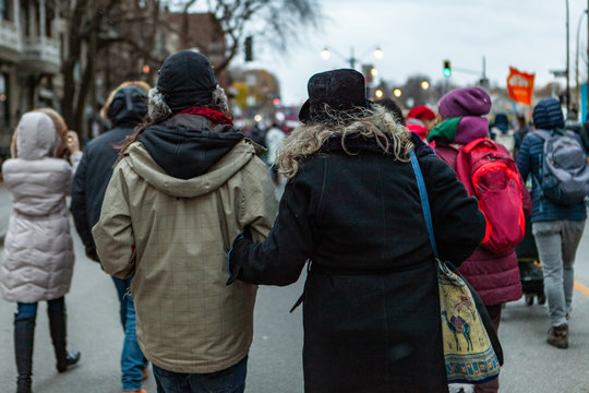 Environmental Activists March In City. Ecological Protestors Are Viewed From Behind During A Street Demonstration, Wearing Winter Clothes And Linking Arms, Unity During A Rally Against Climate Change