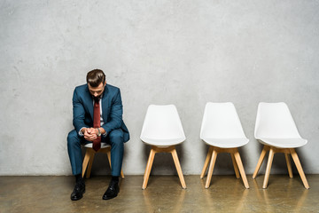 Fototapeta premium handsome man sitting with clenched hands on white chair while waiting job interviw