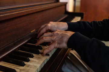 Elderly person plays music on piano. A close-up view on the arthritic hands of an old man playing a melody on an antique wooden piano. Worn keys are seen in the foreground with copy-space.