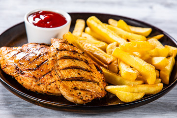 Grilled chicken fillets with french fries on wooden table
