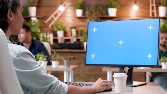 Woman typing on a computer with a blue screen mock-up in modern and cozy office