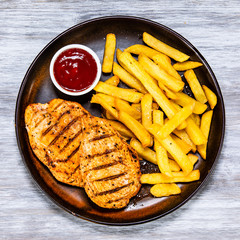 Grilled chicken fillets with french fries on wooden table