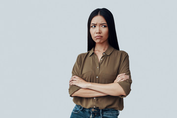 What can I do? Confused young Asian woman making a face while standing against grey background