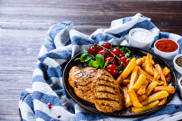 Grilled chicken fillet with french fries on wooden table - obrazy, fototapety, plakaty