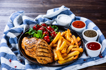 Grilled chicken fillet with french fries on wooden table