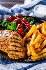 Grilled chicken fillet with french fries on wooden table