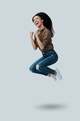 Fototapeta na wymiar Success. Full length of beautiful young Asian woman gesturing and smiling while hovering against grey background