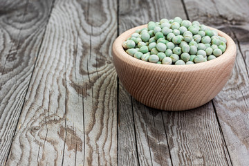 Dried green peas in wooden bowl on wooden background. Peas in a bowl. Natural decoration with green pea.