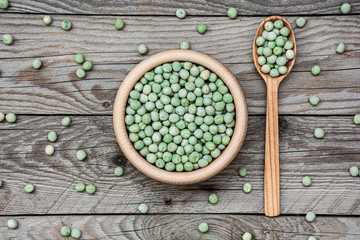 Flat lay photo of dried green peas in wooden bowl on wooden background with spoon. Legumes in a bowl. Natural decoration with green pea.