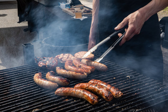 Organic produce sold at farmer's market. A close up view of a man using tongs to turn sausages over a bbq grill with rising steam, preparing hot food to be served at a local outdoor fair.