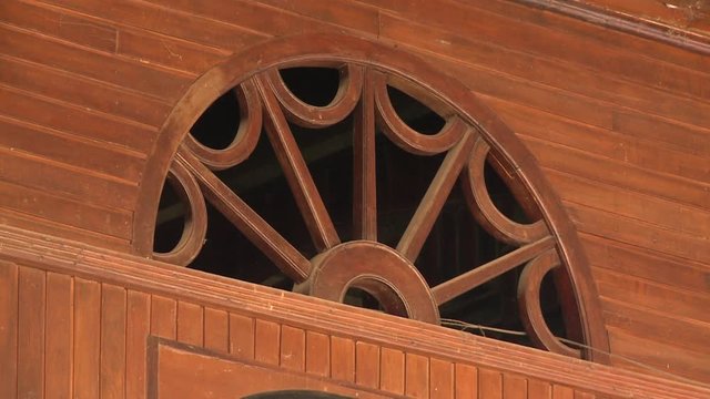 A daylight closeup shot of a half-round five-spoke wagon-wheel style window transom made of wood and embedded in a wooden wall siding.