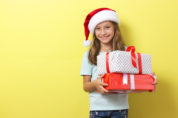 cute cheerful girl in a Christmas hat on a colored background holding gifts in her hands