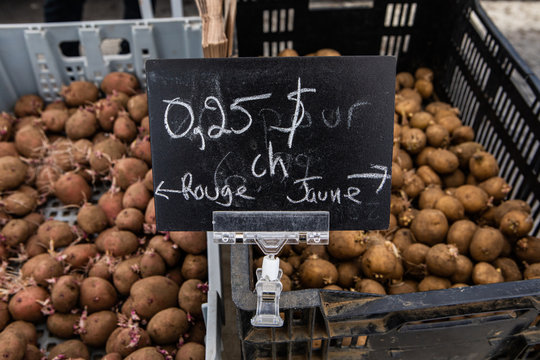 Organic produce sold at farmer's market. A French price sign is seen closeup showing yellow & red potatoes for sale at a fair for local farmers, blurry baskets filled with spuds are seen in background