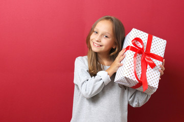 cute cheerful girl in a Christmas hat on a colored background holding a gift