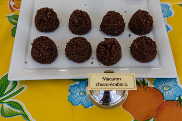 Organic produce sold at farmer's market. A close-up view of chocolate and maple flavored macaroons, served on a white dish at an outdoor fair for local food producers, with a small French label.