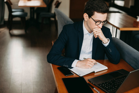 Adult confident seriously manager sitting in a coffee shop at lunch time thinking and working dressed in suit .