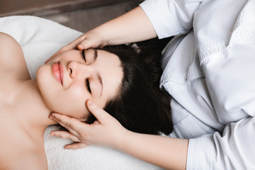 Side view portrait of a amazing caucasian woman leaning on a spa bed with closed eyes having facial skincare therapy by a cosmetologist in a wellness spa center