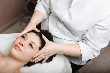 Obraz na płótnie Canvas Upper view of a attractive caucasian female doing skin care facial massage while leaning on a spa bed with eyes opened in a wellness center.