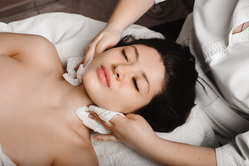 Upper view of a young attractive woman doing anti acnee procedures in wellness spa resort by a female cosmetologist.