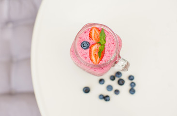 Pink strawberry smoothie in glass with mint leaves on white table.