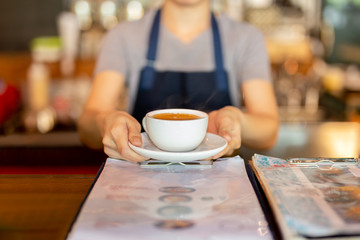 Fototapeta na wymiar Waitress serving coffee while standing in coffee shop counter.