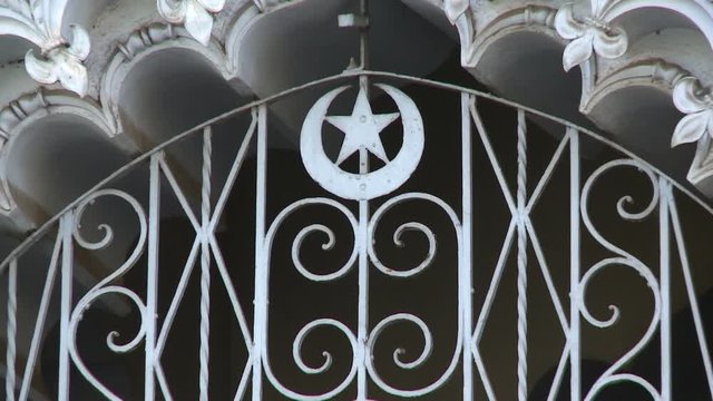 A hand held, close-up shot of a white gate decorated with a star and a moon.