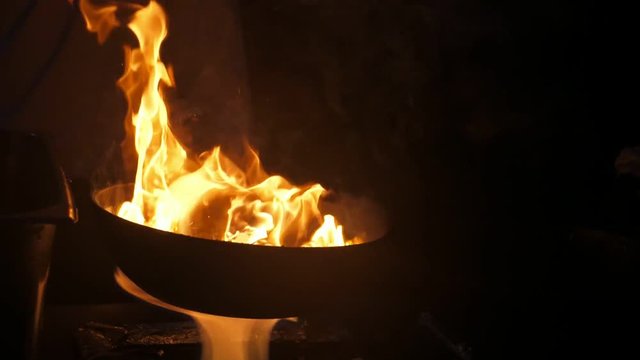 Forks of fire playing on a frying pan kept by chef at outdoor kitchen in slo-mo