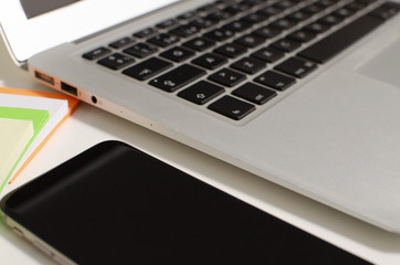 Laptop and phone on a table with infinite white background with note pots.