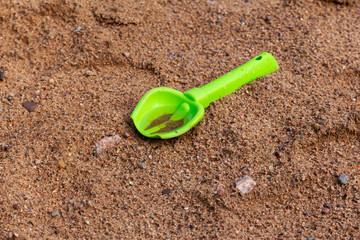 green baby shovel on the wet yellow sand. Forgotten toy after rain in the sandbox