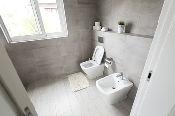 Fototapeta na wymiar Half-open door to luxury bathroom with white ceramic bidet and toilet