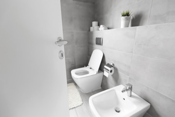 Half-open door to luxury bathroom with white ceramic bidet and toilet