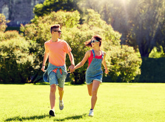 holidays, vacation, love and people concept - happy smiling teenage couple holding hands and running at summer park