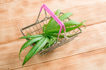 Fresh leaves of marijuana in a grocery basket on a wooden background. Cannabis trade, marijuana production concept.