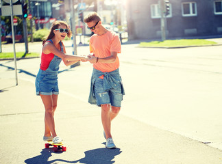 summer holidays, extreme sport and people concept - happy teenage couple riding short modern cruiser skateboard on city street