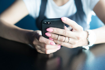 Well-groomed hands of the girl with pink manicure hold the smartphone. A girl using a smartphone dials a message or makes an online payment or posts a story in the social network