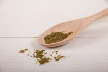 Moringi powder in a wooden spoon on a light background.