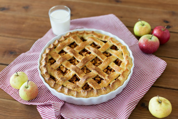 food, culinary and baking concept - apple pie, glass of milk and kitchen towel on wooden table