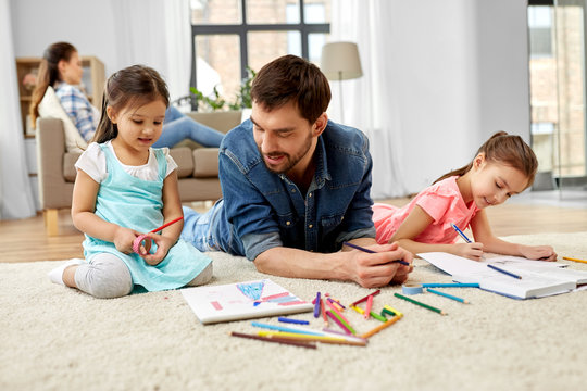 family, motherhood and leisure concept - father spending time with her little daughters drawing and helping with homework lying on floor at home