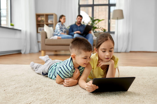 childhood, technology and family concept - brother and sister with tablet computer lying on floor at home