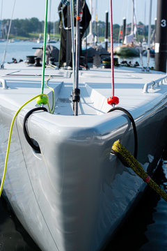White bow of 12-Meter racing sailboat with red and green halyards and yellow dock lines in slip in marina.