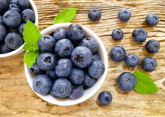 Bowl of fresh blueberries on rustic wooden old table. Freshly picked blueberries in bowl. Healthy organic fruit background. Organic food raw blueberries and mint leaf for healthy lifestyle.