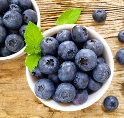 Bowl of fresh blueberries on rustic wooden old table. Freshly picked blueberries in bowl. Healthy organic fruit background. Organic food raw blueberries and mint leaf for healthy lifestyle.