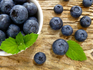 Bowl of fresh blueberries on rustic wooden old table. Freshly picked blueberries in bowl. Healthy organic fruit background. Organic food raw blueberries and mint leaf for healthy lifestyle.