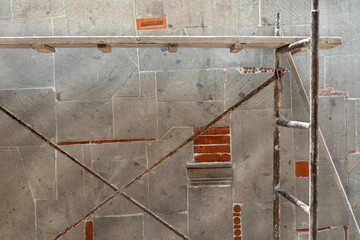 Scaffold used to climb in constructions. Mixed quarry stones in a brick wall
