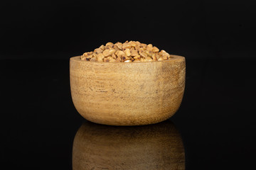 Lot of whole raw brown buckwheat grain in a wooden bowl isolated on black glass