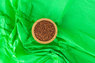 Lot of whole hulled raw red quinoa seeds in a wooden bowl flatlay on a crumpled green paper