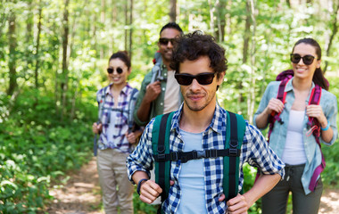 travel, tourism, hike and people concept - group of friends walking with backpacks in forest