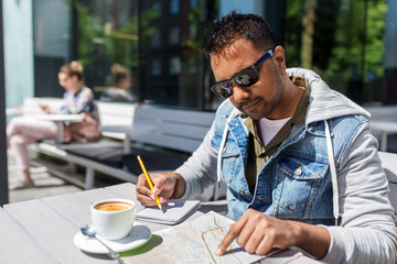 travel, tourism and people concept - indian man with map, notebook and coffee at street cafe in city